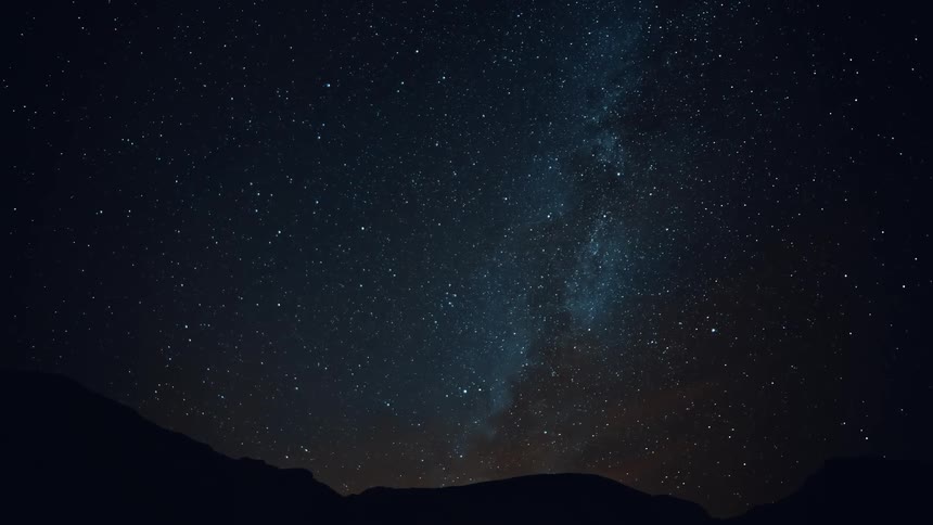 The stars of the milky way glow in the darkness as they move over mountains