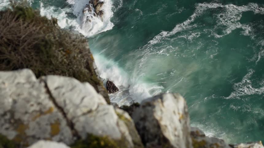 Waves roll onto shore past a cliff ledge