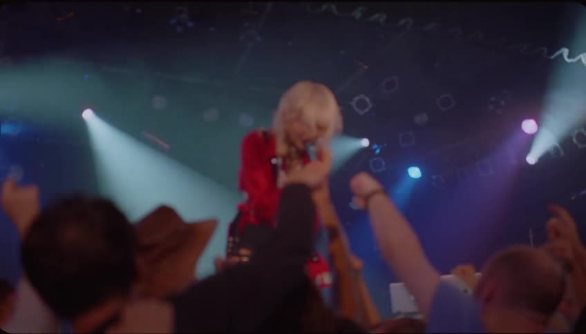 A woman on stage is singing to the audience that is enjoying it and raising their arms up