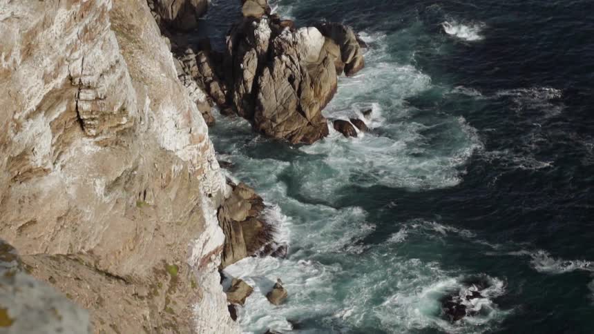 Ocean waves crash at the base of a rocky cliff