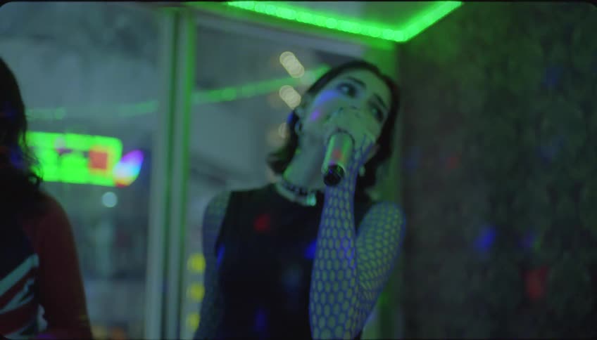 Two women sing karaoke while watching screen