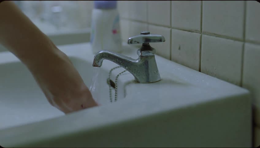 A woman turns on the tap to wash her hands in a welllit bathroom