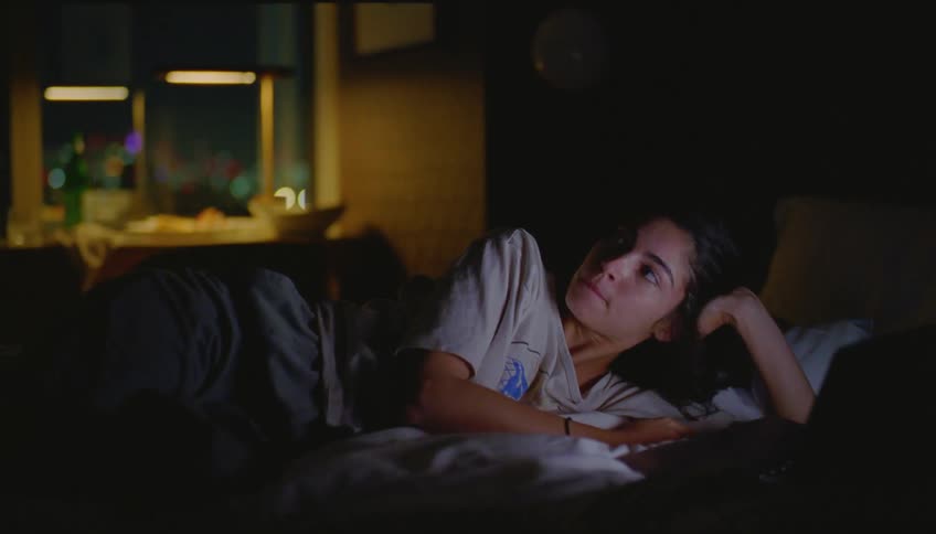 Woman lying on the bed watching something on the laptop in the dark room until she closes the lid and stands up