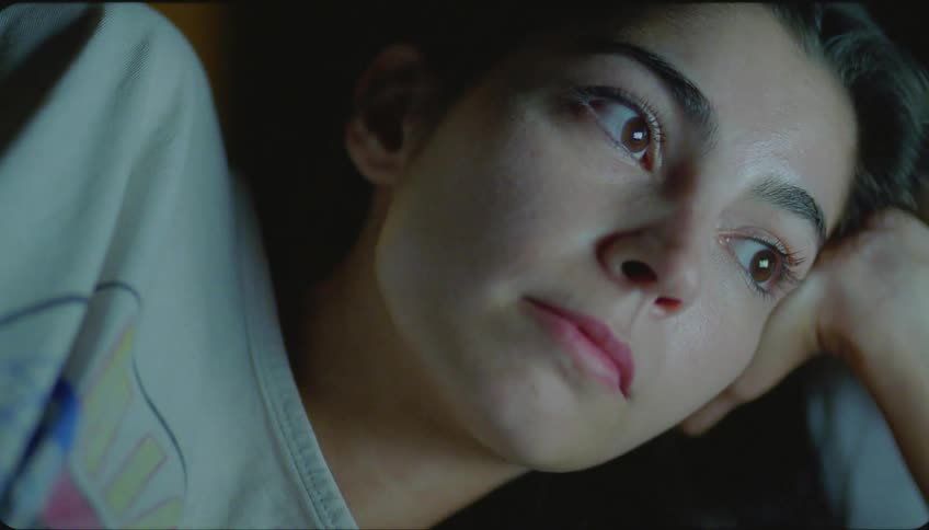 Young woman lying in bed watching a movie on a laptop