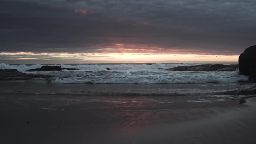 Waves crash against the beach at sunset