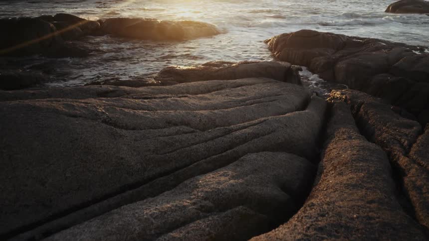 The sun sets over a rocky ocean shore
