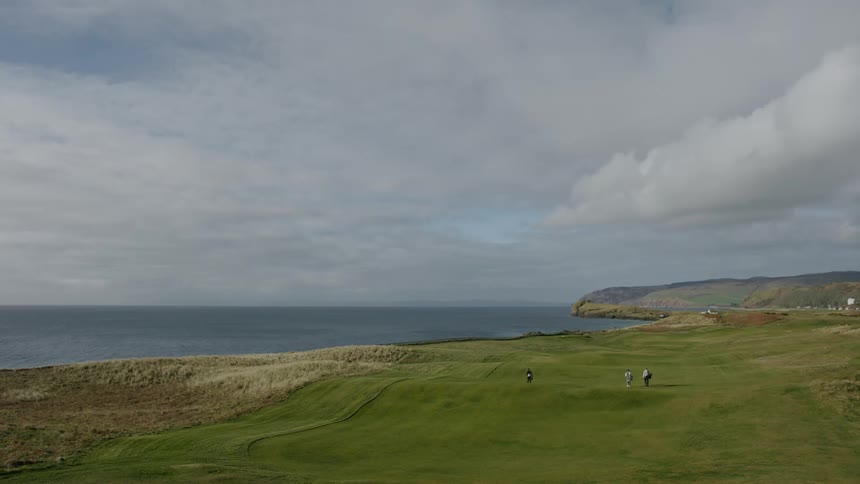 People walking on a golf course next to the ocean