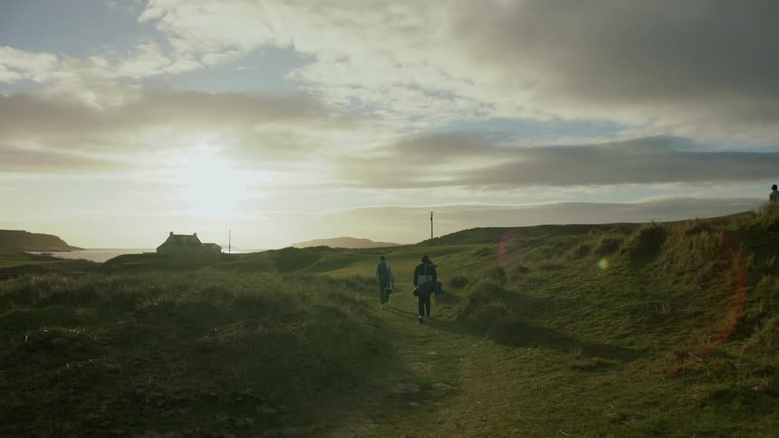 People carrying bags walk along path toward house on coast on a cloudy day