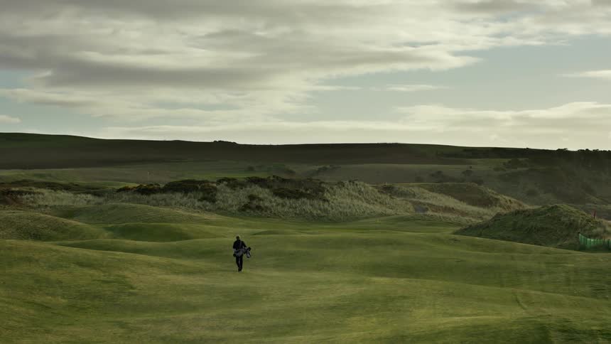 A man walking alone on a golf course during the day