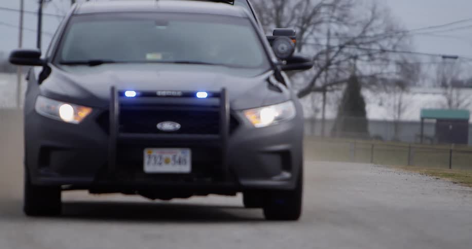 A motorcade of police vehicles pass by with their lights flashing