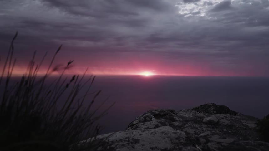 The sun sets over the ocean with storm clouds and a lightning strike