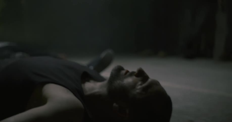 A man lies on the floor of a dim room