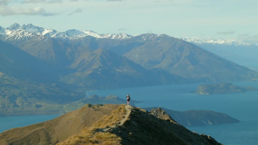 A person stands on the peak of a large hill