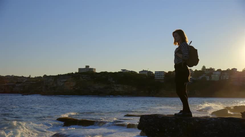 A woman is standing near the rough waters