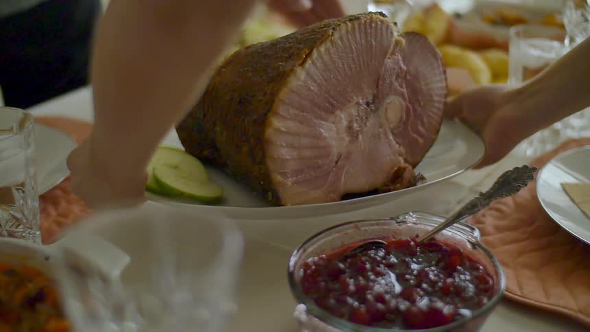 Person setting cooked ham on dinner table