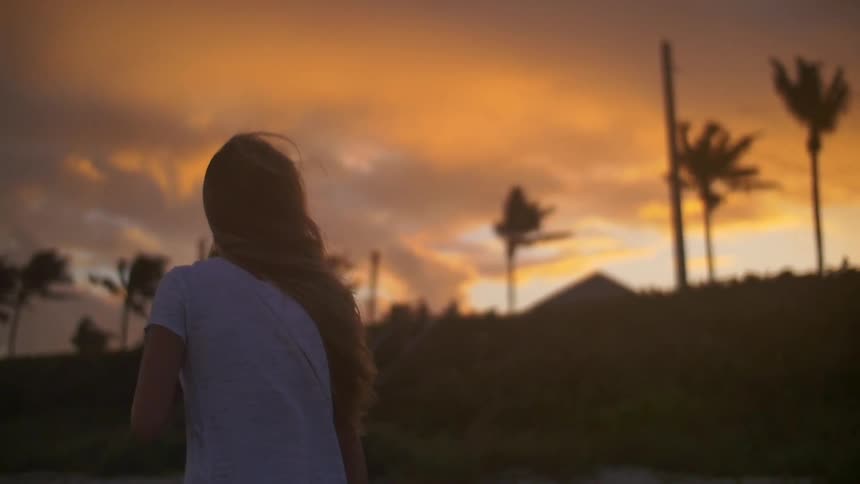 A woman walks outside in the heavy wind at sunset
