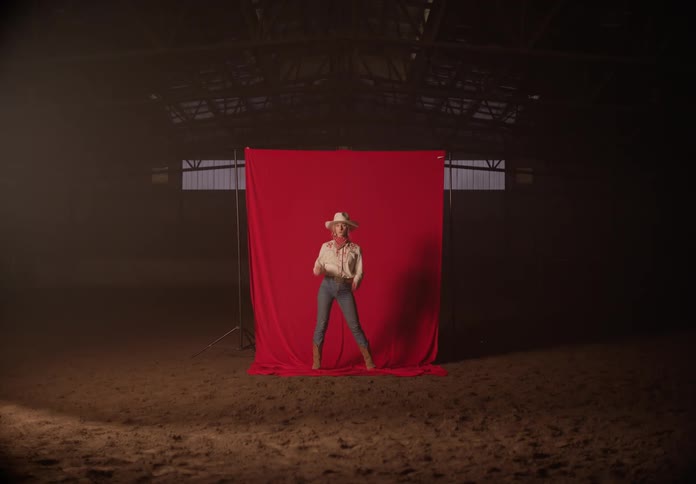 Woman modeling as a cowgirl against a red backdrop inside a rodeo arena