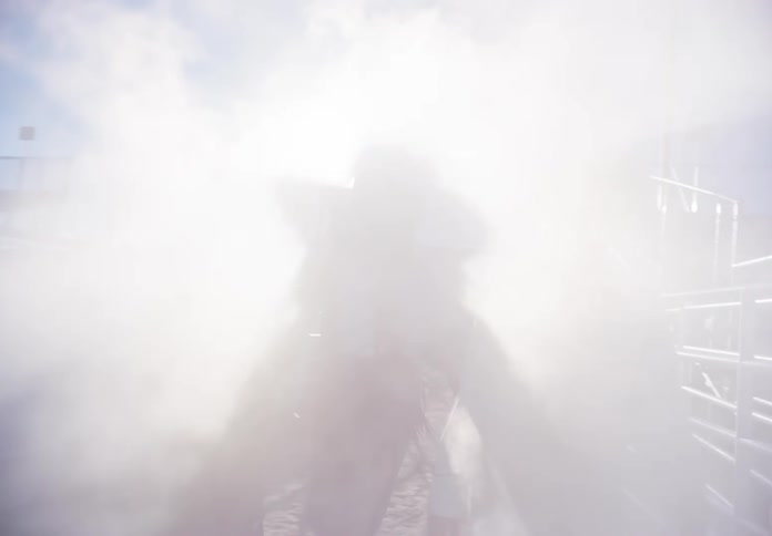 Three models dressed as cowgirls walking inside a rodeo arena with smoke passing beneath them
