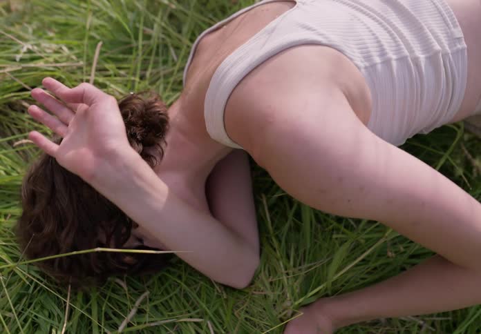 A sad woman lying in a meadow during the day