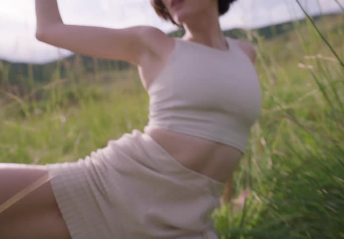 A young white woman is sitting on the grass outdoor showing her dance move