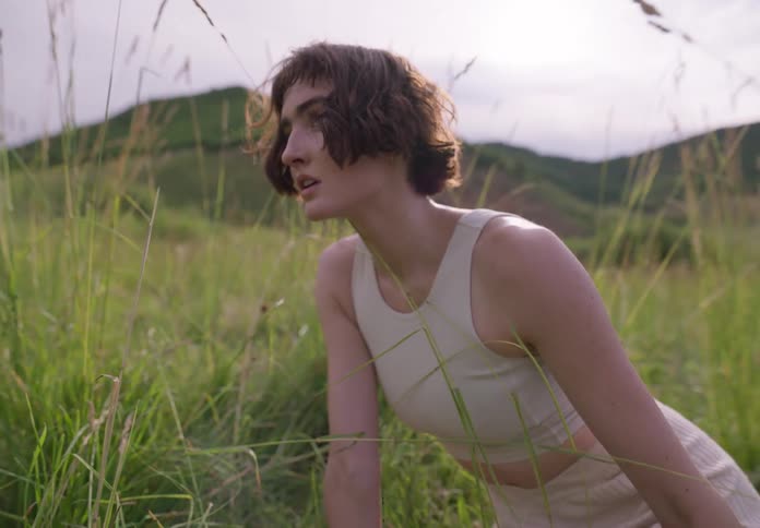A lady sit alone on grass field near a hill at daytime