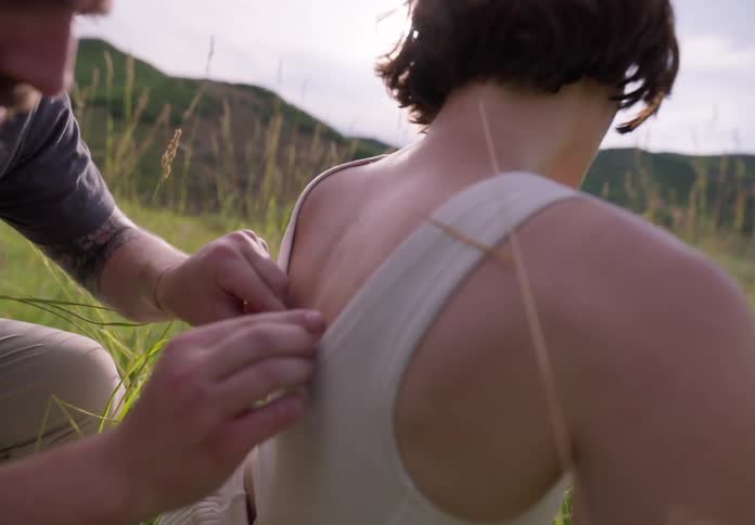 A man picking up grass from a womans back as she sits on the grass