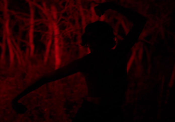 Silhouette of a woman dancing in a forest at night with red light