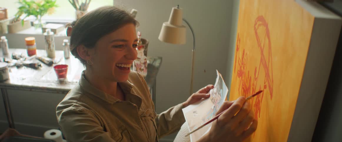 Portrait of a painter painting on a canvas with a brush observing an image in her other hand