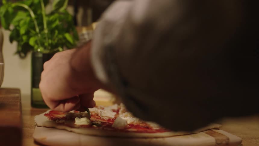 Closeup of a mans hands picking up basil leaves and placing them on top of the pizza