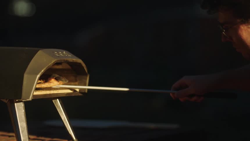 A man taking a pizza out of an outdoor oven