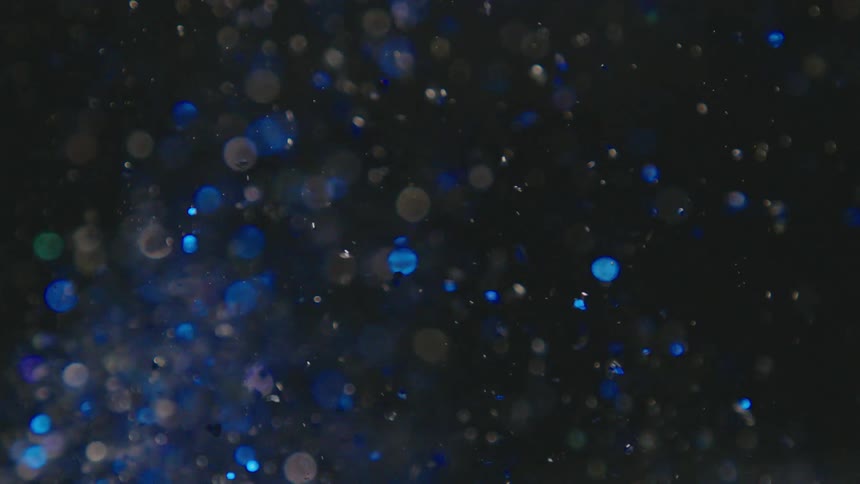Extreme closeup of a jet of water with bubbles amidst abstract blue sequins