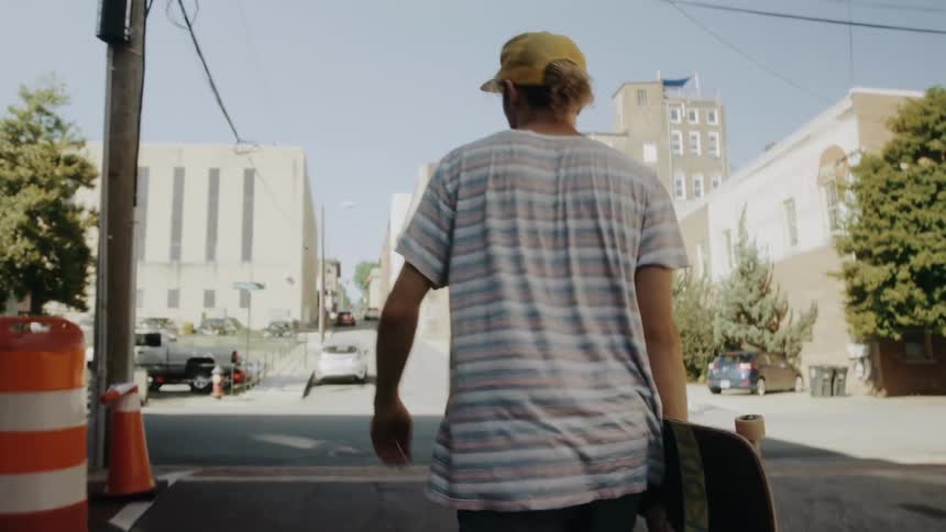 A man walking through the streets of a neighborhood with a skateboard in his hands
