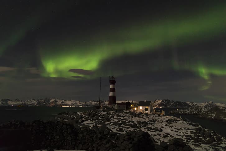 Landscape of snowy terrain with a house and an observation tower in the arctic under a night sky with the northern lights