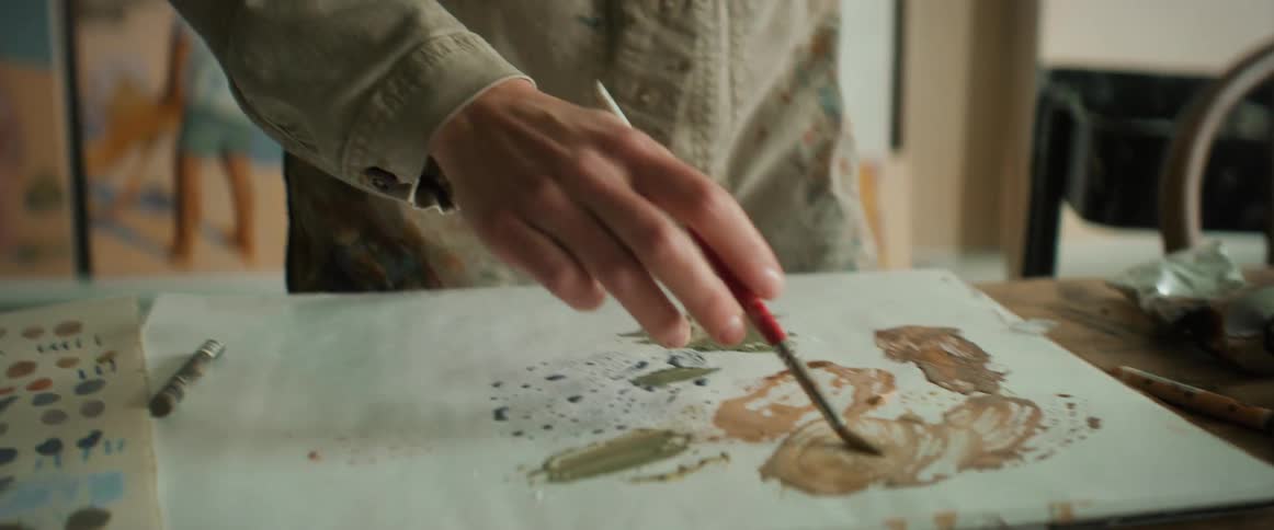 Closeup of a painters hands holding a brush and mixing paint colors on a white canvas