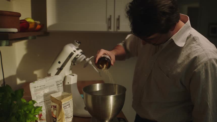 Man shakes ingredient into mixing bowl in kitchen