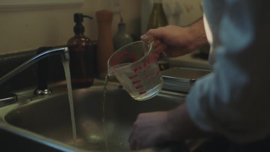 A person in the kitchen turning water into a glass jar