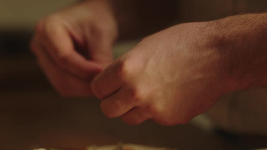 Closeup of a mans hands putting ingredients on a pizza