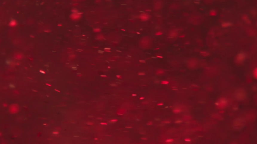 Extreme closeup of water with red confetti spinning in slow motion