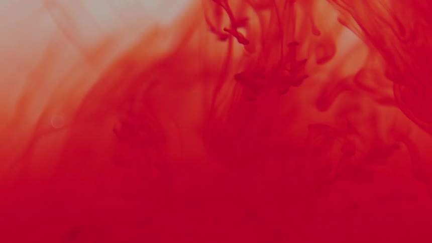 Extreme closeup of red ink fluid blending abstractly in slow motion