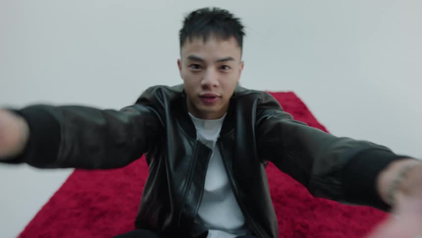 Male model sitting on a red carpet making hand gestures facing the camera
