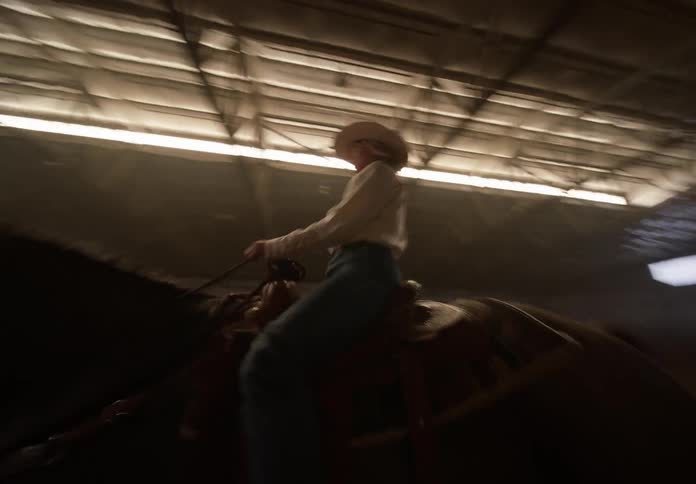 Shaky footage of a cowgirl riding a horse inside a hangar