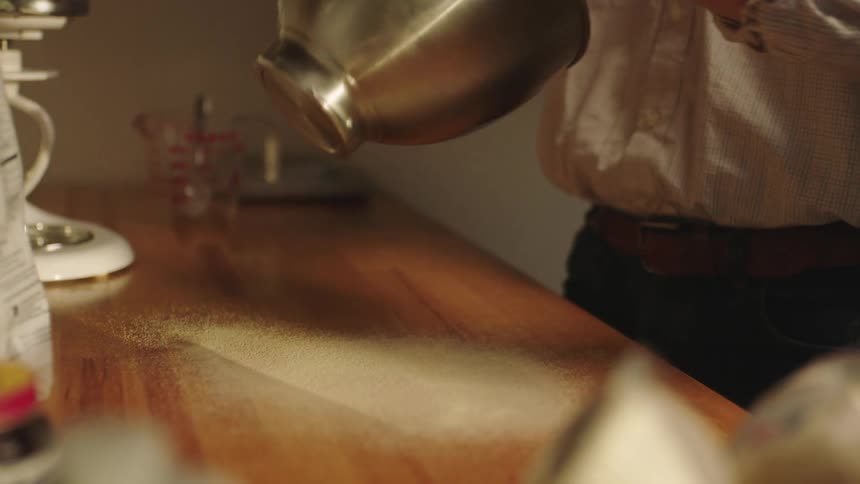A man spreading flower on a kitchen table to knead dough on