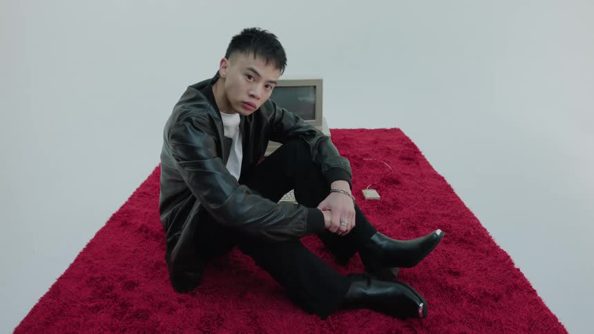A man sitting on a red wooly carpet in an all white room in front of an old computer