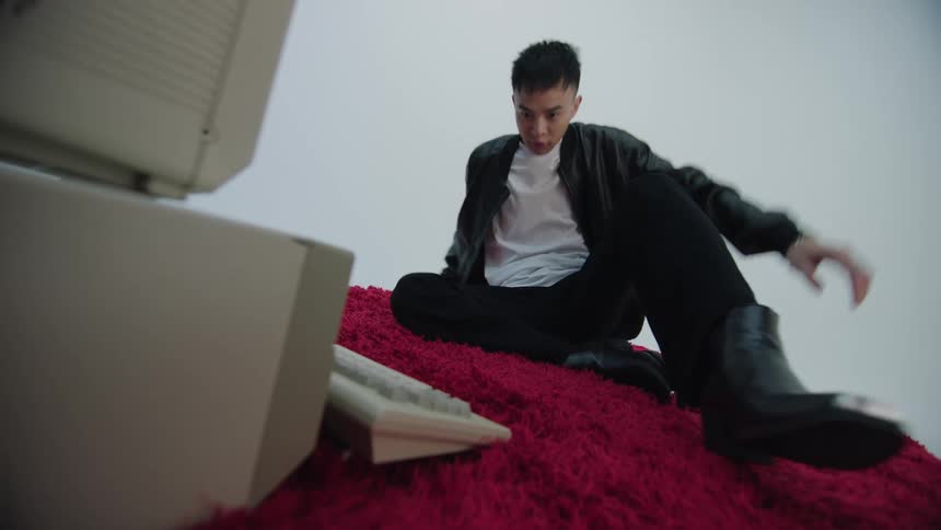 Young man sitting on a red carpet kicks the keyboard of a computer