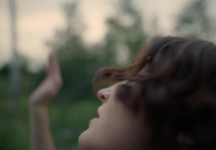 A woman wearing a crop top dances gracefully in a grassy landscape