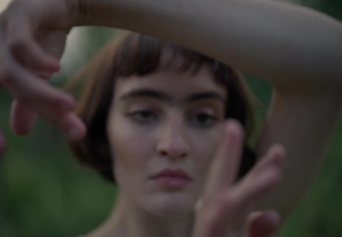 Woman with bob hairstyle and a white shirt dances in the green field