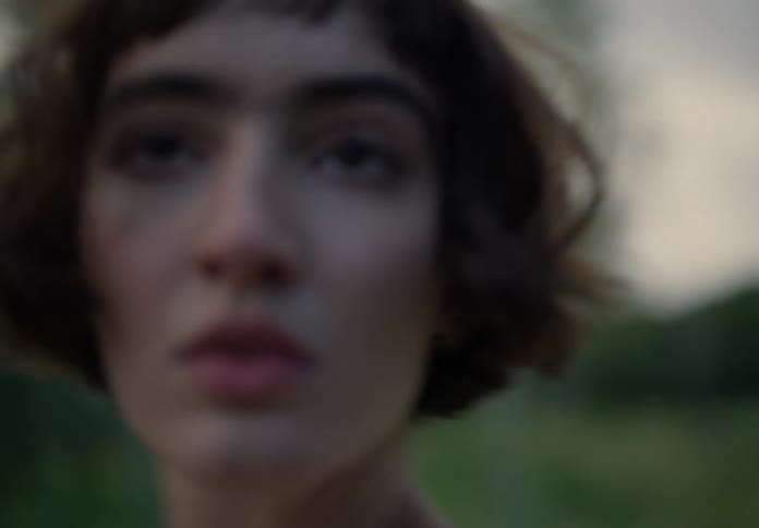 A woman with a bob hairstyle and a crop top dances freely in a grassy expanse