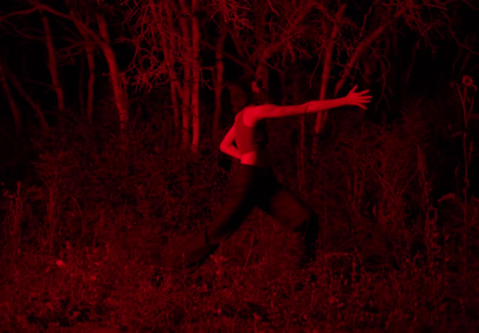 Woman dancing in the forest at night with a red light shining on her