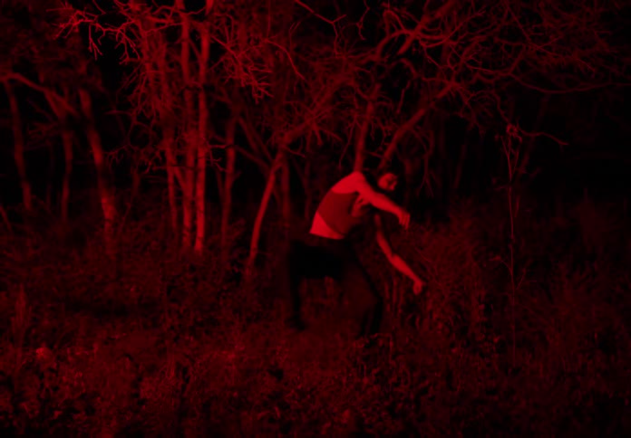 Woman dancing scenically in the middle of a forest at night with red lighting