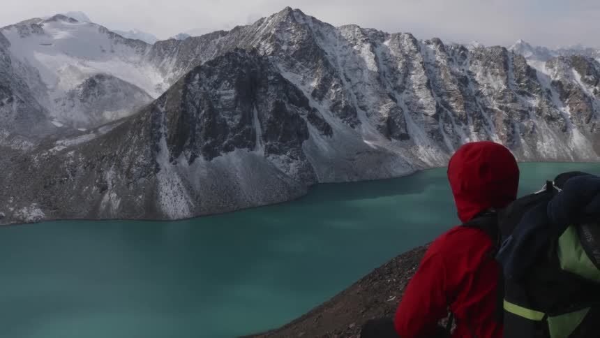 A person wearing red warm clothing is looking at a snowcovered mountain in front of a large lake